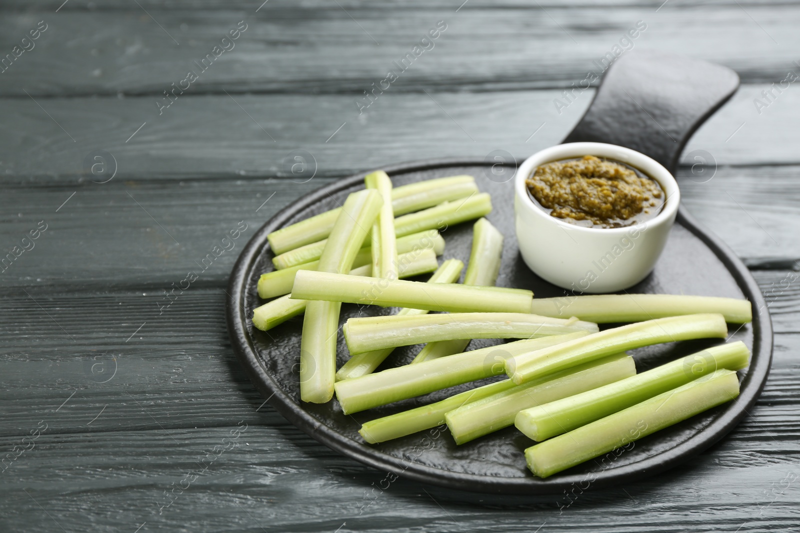 Photo of Slate board with celery sticks and dip sauce on grey wooden table
