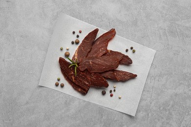 Pieces of delicious beef jerky and spices on light grey table, top view
