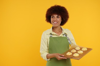 Photo of Happy young woman in apron holding board with cookies on orange background. Space for text