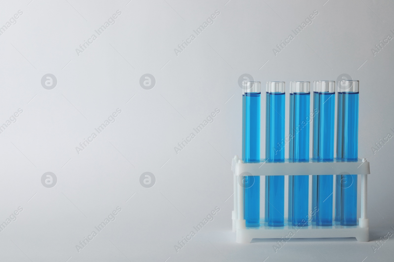 Photo of Test tubes with blue liquid on light grey background. Space for text