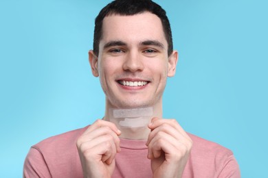 Photo of Young man with whitening strips on light blue background