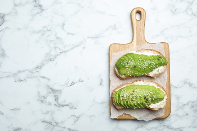 Photo of Tasty avocado sandwiches on white marble table, top view. Space for text