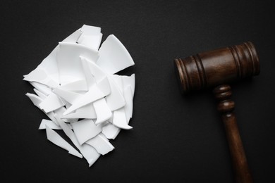Divorce concept. Pieces of broken plate and wooden gavel on black background, flat lay