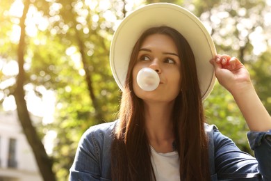 Photo of Beautiful young woman blowing chewing gum outdoors