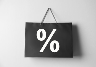 Image of Black paper shopping bag with percent sign hanging on white wall. Discount concept