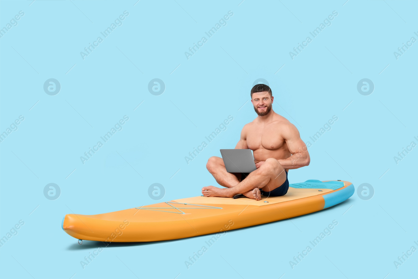 Photo of Man with laptop on SUP board against light blue background