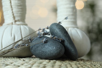 Photo of Spa composition. Herbal bags, stones and dry lavender flowers on wicker mat, closeup