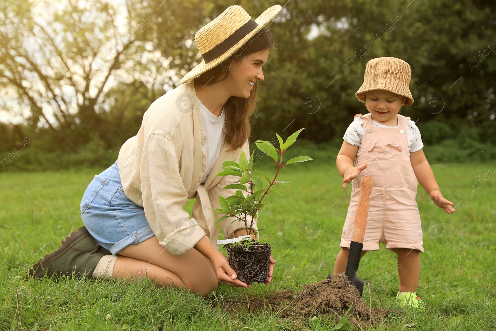 Photo of Mother and her baby daughter planting tree together in garden