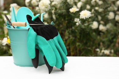 Photo of Gardening gloves and bucket with different tools on white wooden table outdoors, space for text