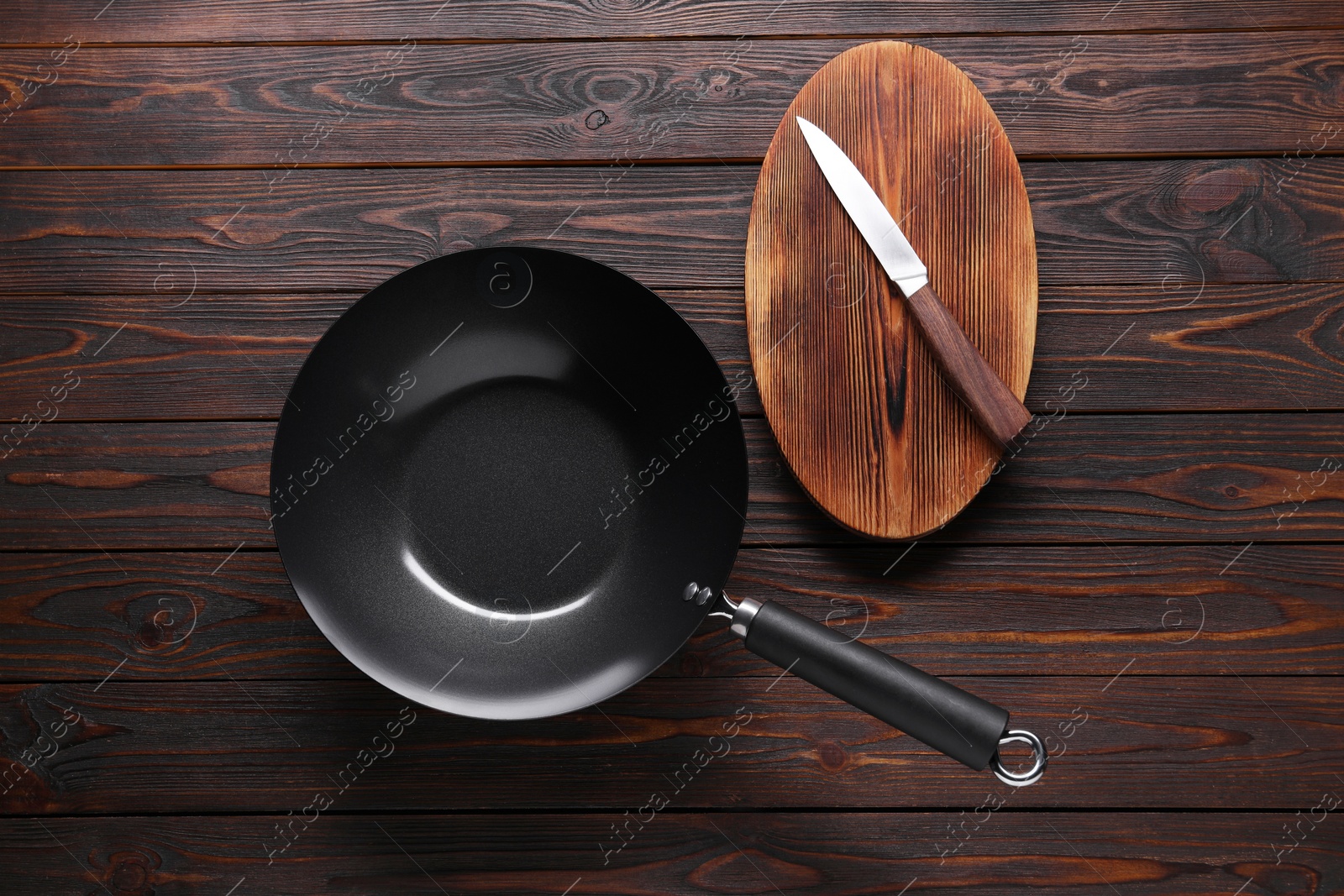 Photo of Empty iron wok, knife and cutting board on wooden table, flat lay