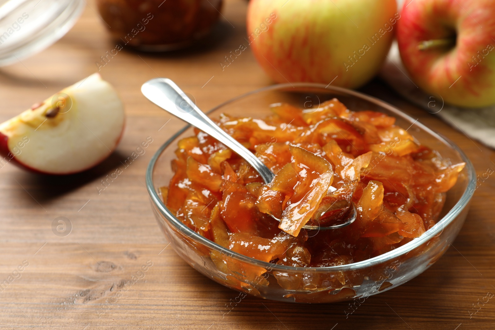 Photo of Tasty apple jam in glass bowl and fresh fruit on wooden table, closeup