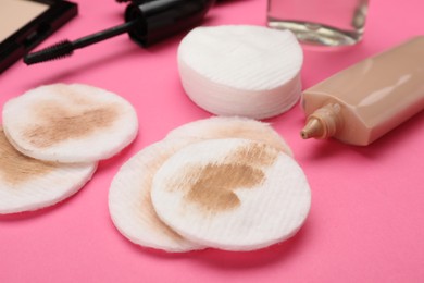 Dirty cotton pads after removing makeup and different cosmetic products on pink background, closeup