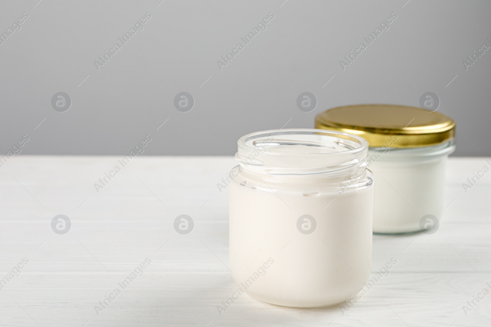 Photo of Jars with delicious organic yogurt on white wooden table, closeup. Space for text