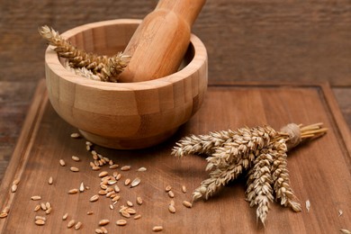 Mortar, pestle and ears of wheat on wooden table