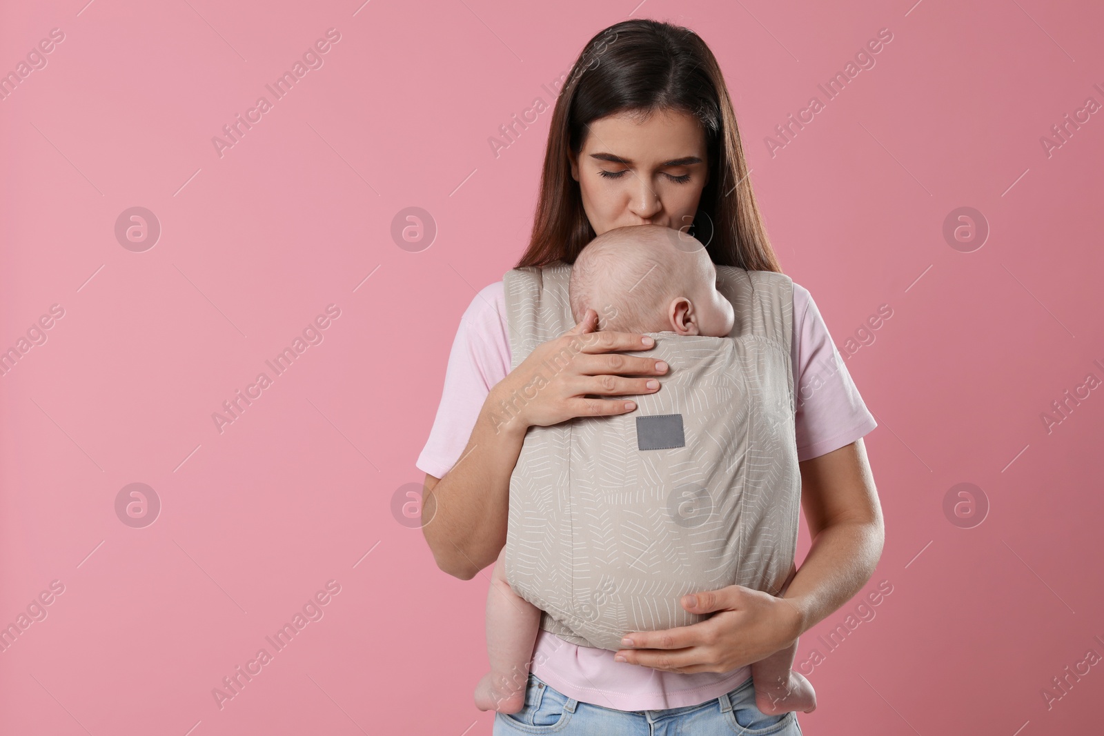 Photo of Mother holding her child in sling (baby carrier) on pink background. Space for text