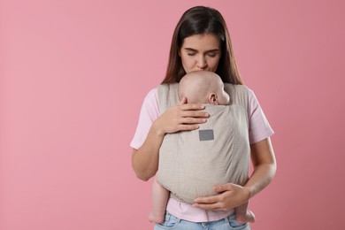 Photo of Mother holding her child in sling (baby carrier) on pink background. Space for text