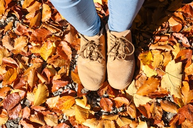 Photo of Woman standing on ground covered with fallen autumn leaves, top view