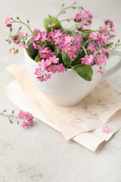 Photo of Beautiful pink forget-me-not flowers with cup on light stone table