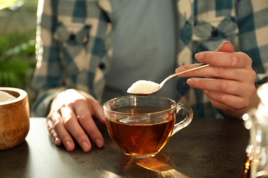 Photo of Woman adding sugar into cup of tea at dark table, closeup
