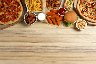 French fries, pizza and other fast food on wooden table, flat lay with space for text