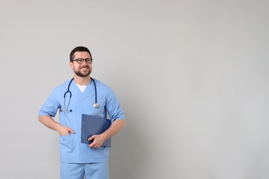 Photo of Smiling doctor with clipboard and stethoscope on light grey background. Space for text