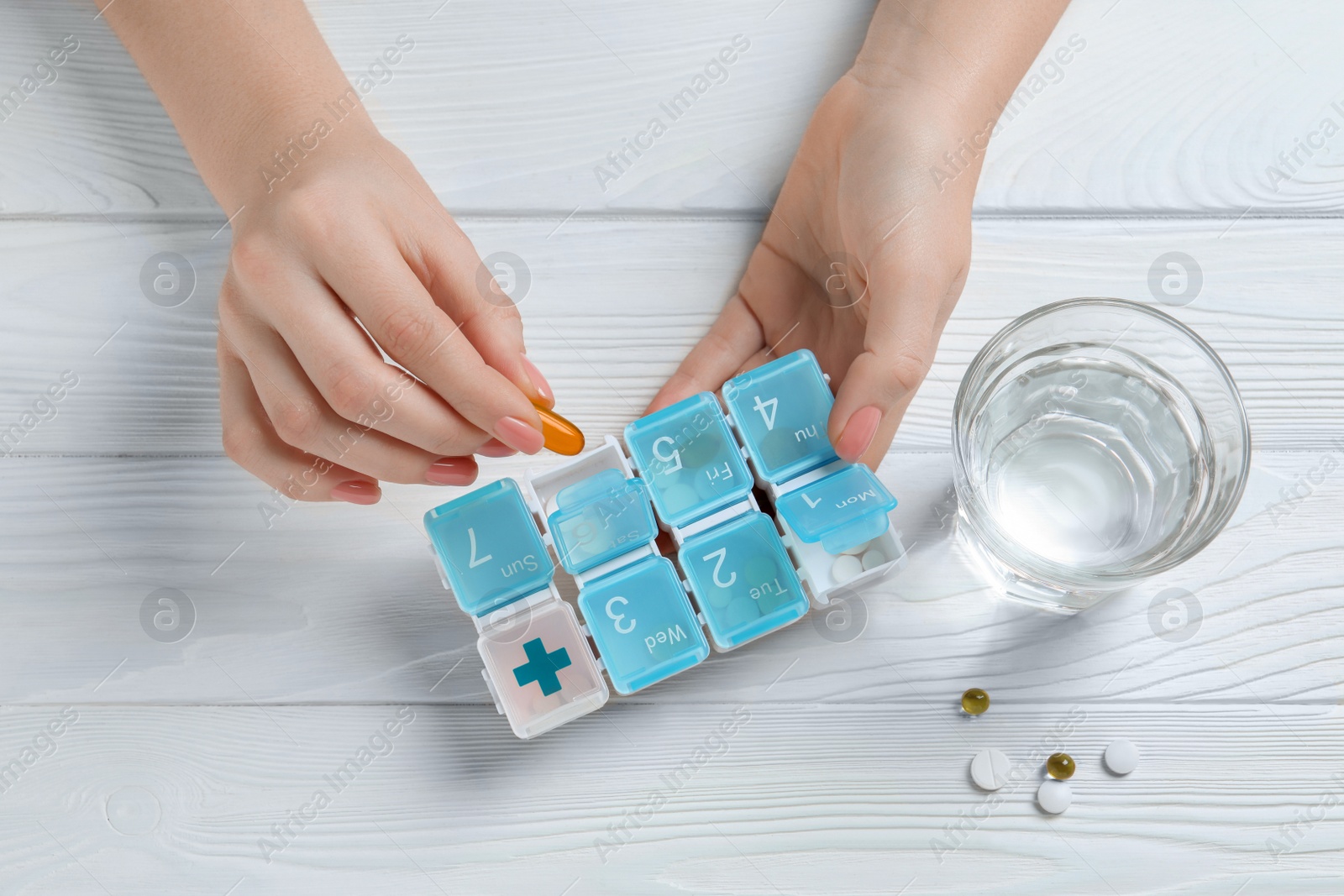 Photo of Woman putting pill into weekly organizer at wooden white table, top view