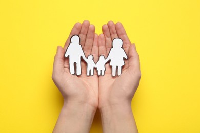 Photo of Woman holding paper family cutout on yellow  background, top view