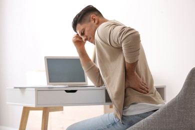 Photo of Man suffering from back pain at workplace. Bad posture problem