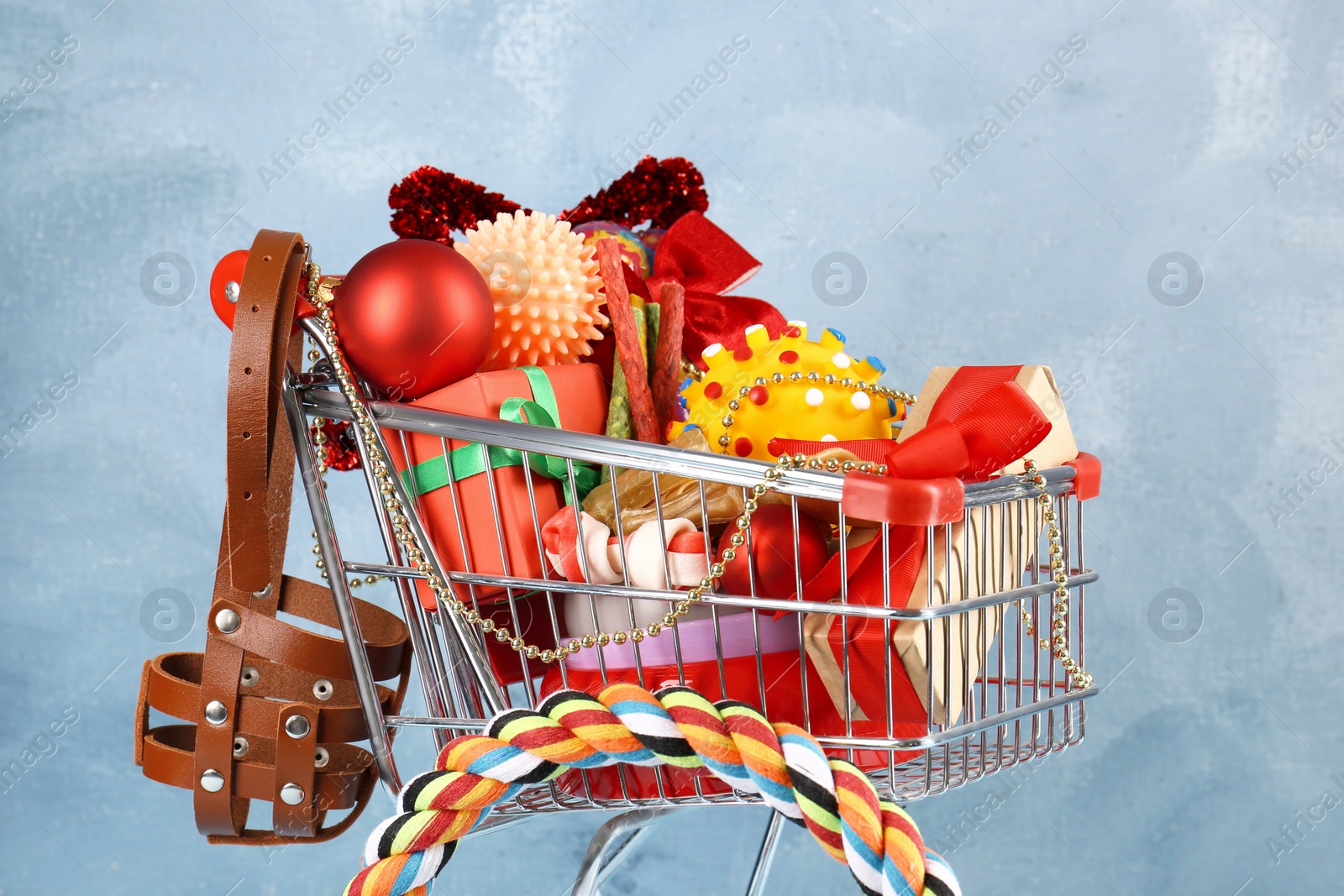 Photo of Small shopping cart with different pet goods and Christmas gifts on light blue background. Shop assortment