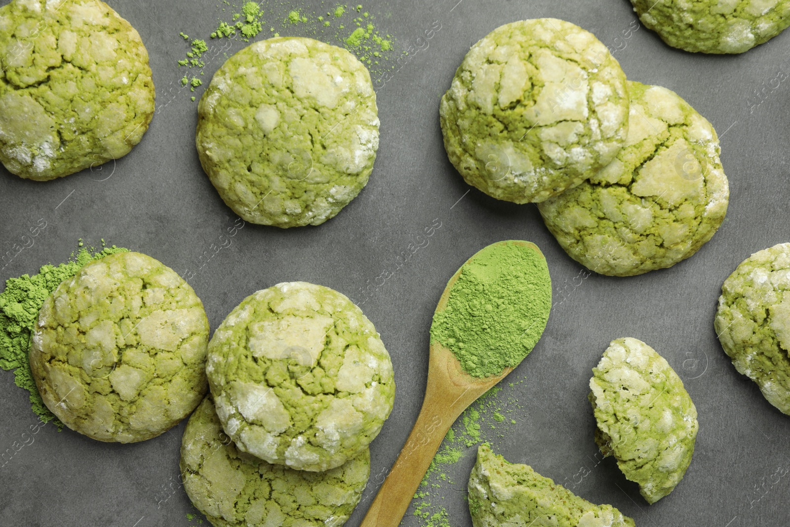 Photo of Tasty matcha cookies and wooden spoon of powder on grey table, flat lay