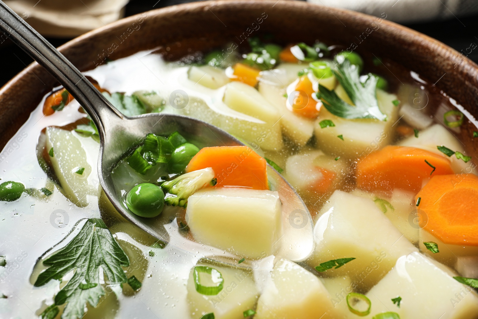 Photo of Spoon of fresh homemade vegetable soup over full bowl, closeup