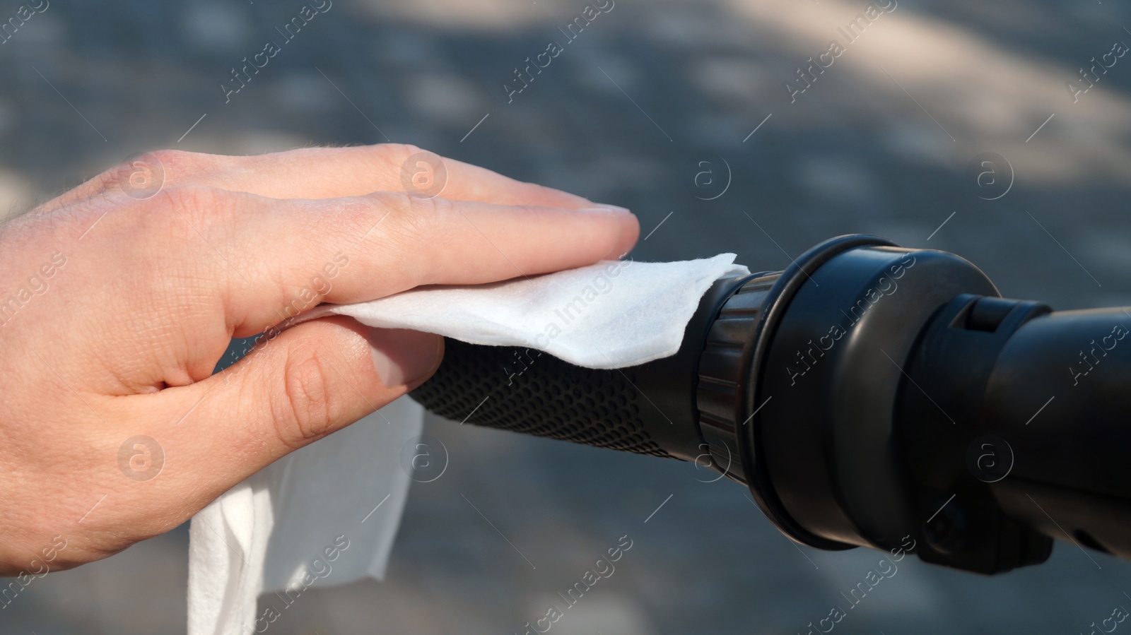 Photo of Man cleaning scooter steering wheel with wet wipe outdoors, closeup. Protective measures