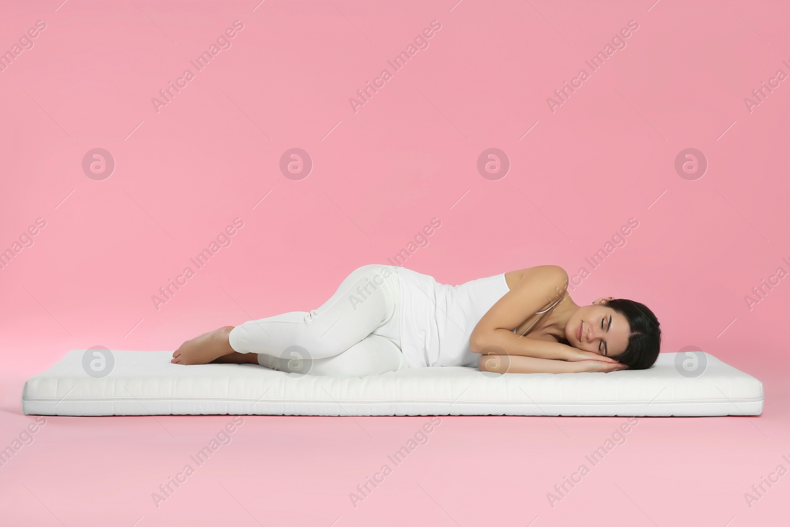 Photo of Young woman lying on soft mattress against pink background