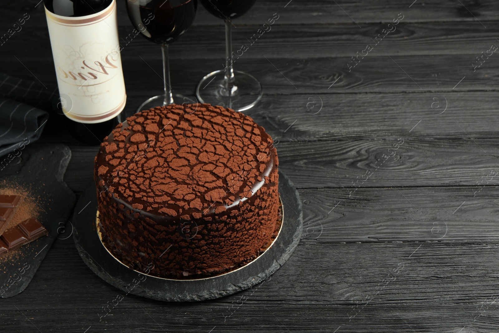 Photo of Delicious truffle cake, chocolate pieces and red wine on black wooden table, space for text