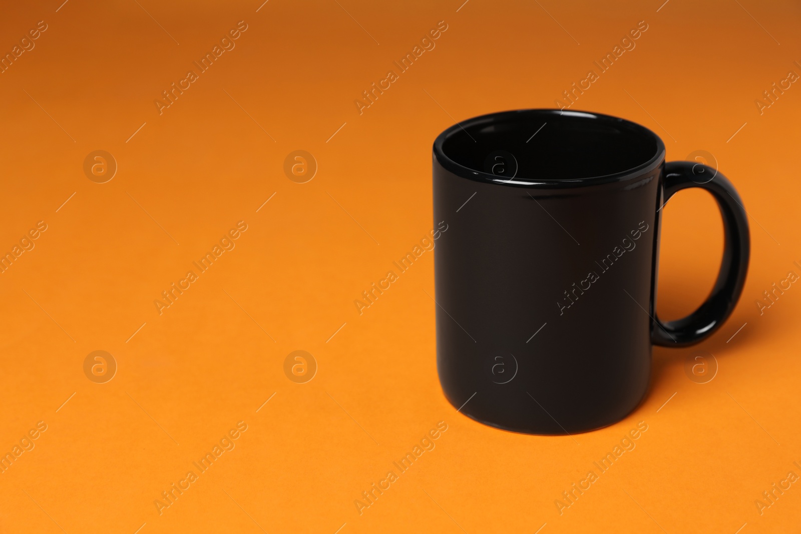 One black ceramic mug on orange background, space for text Photo of One black ceramic mug on orange background, space for text