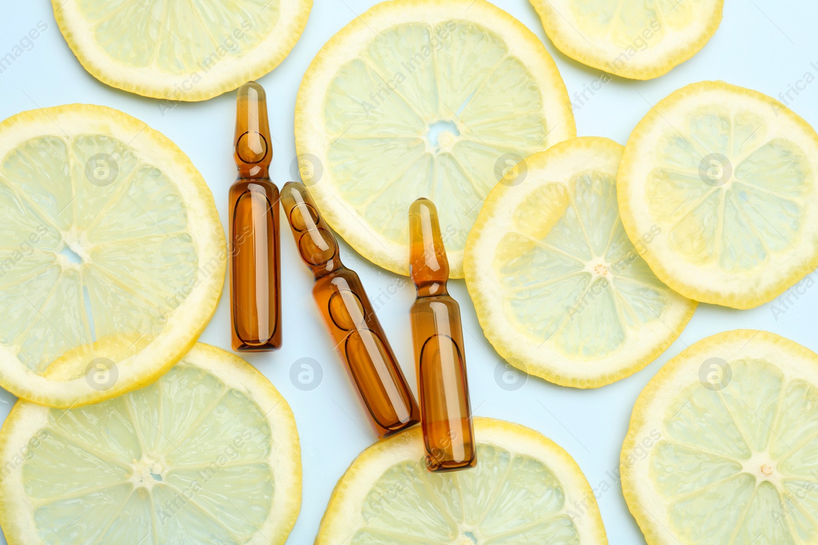 Photo of Skincare ampoules with vitamin C and slices of lemon on light blue background, flat lay