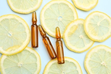 Skincare ampoules with vitamin C and slices of lemon on light blue background, flat lay