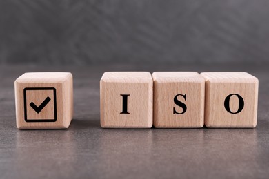 Photo of Wooden cubes with check mark and abbreviation ISO on grey textured table, closeup