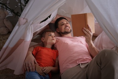 Photo of Father and son reading book in wigwam at home