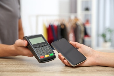 Photo of Woman using payment terminal with smartphone in shop, closeup. Space for text