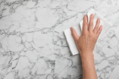 Photo of Woman wiping marble table with paper towel, top view. Space for text