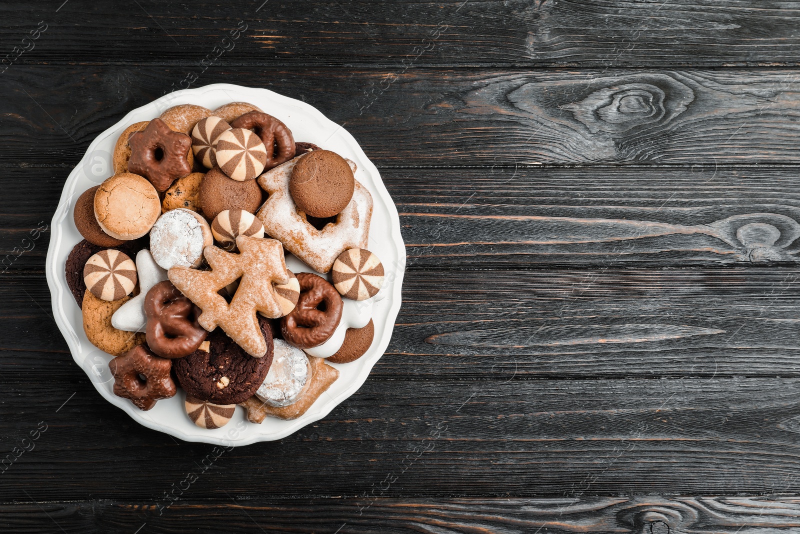 Photo of Delicious cookies in plate on black wooden table, top view. Space for text