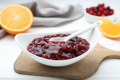 Photo of Fresh cranberry sauce in bowl and spoon on white wooden table, closeup