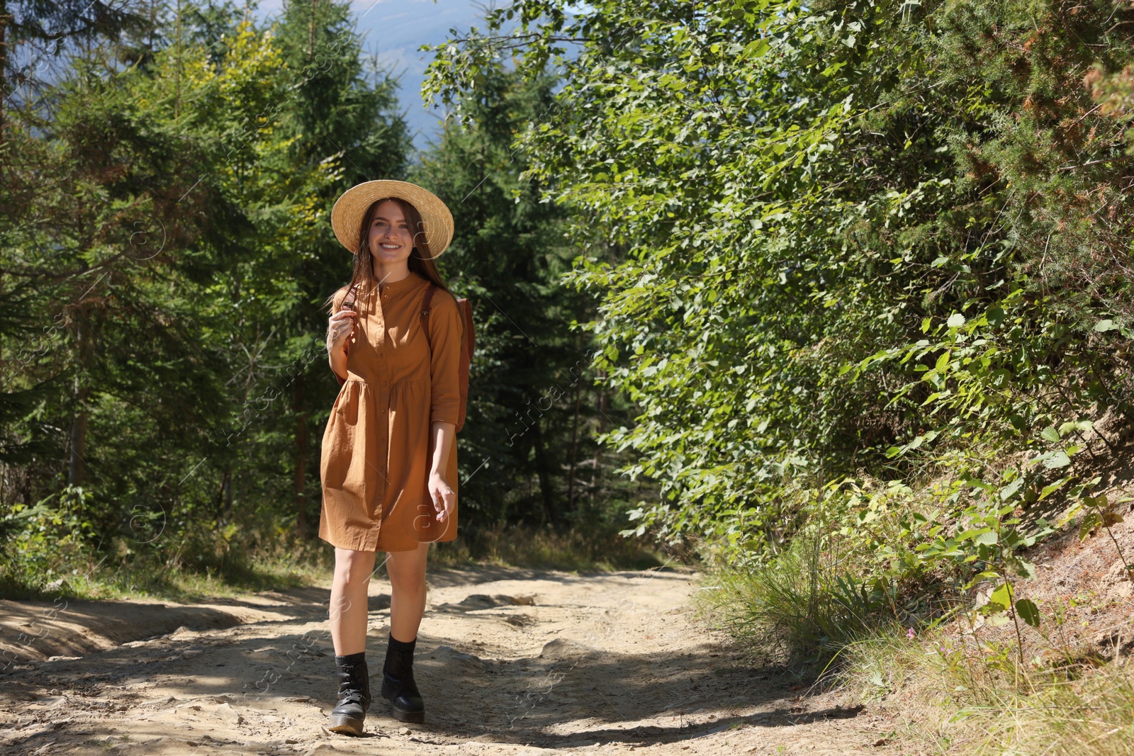 Photo of Happy woman with backpack and hat enjoying her walk in forest