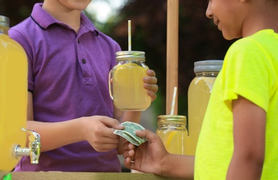 Little boy selling natural lemonade to African-American kid in park, closeup. Summer refreshing drink