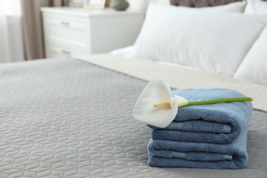 Photo of Stack of clean towels with flower on bed indoors. Space for text