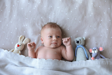 Cute newborn baby with toys in bed, top view