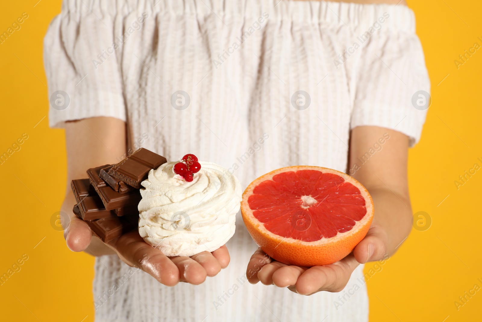 Photo of Concept of choice. Woman holding sweets and grapefruit on yellow background, closeup