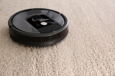 Photo of Modern robotic vacuum cleaner on beige carpet. Space for text