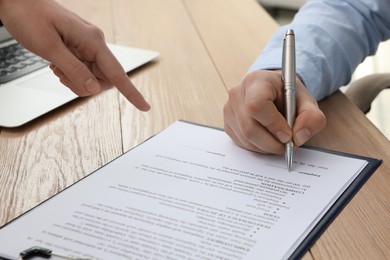 Photo of Businesspeople signing contract at wooden table, closeup